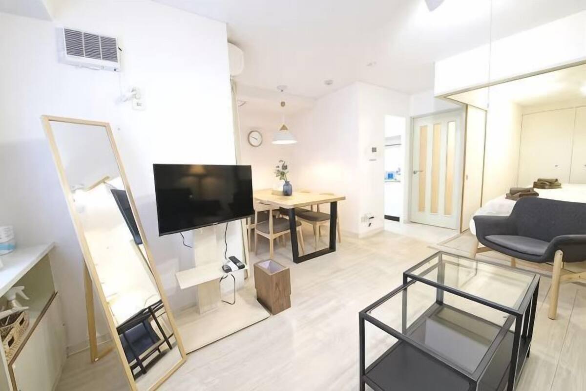 A modern living room with a flat-screen TV, a dining table, a sofa, and a glass coffee table.