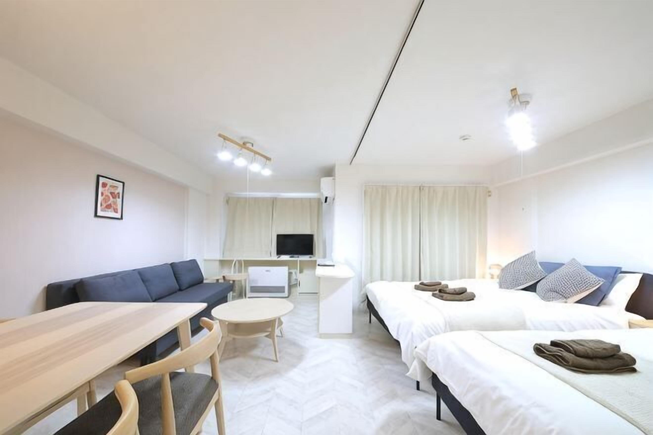 Habitación de hotel con sofá, mesa de comedor, televisión, cama y pequeña cocina.