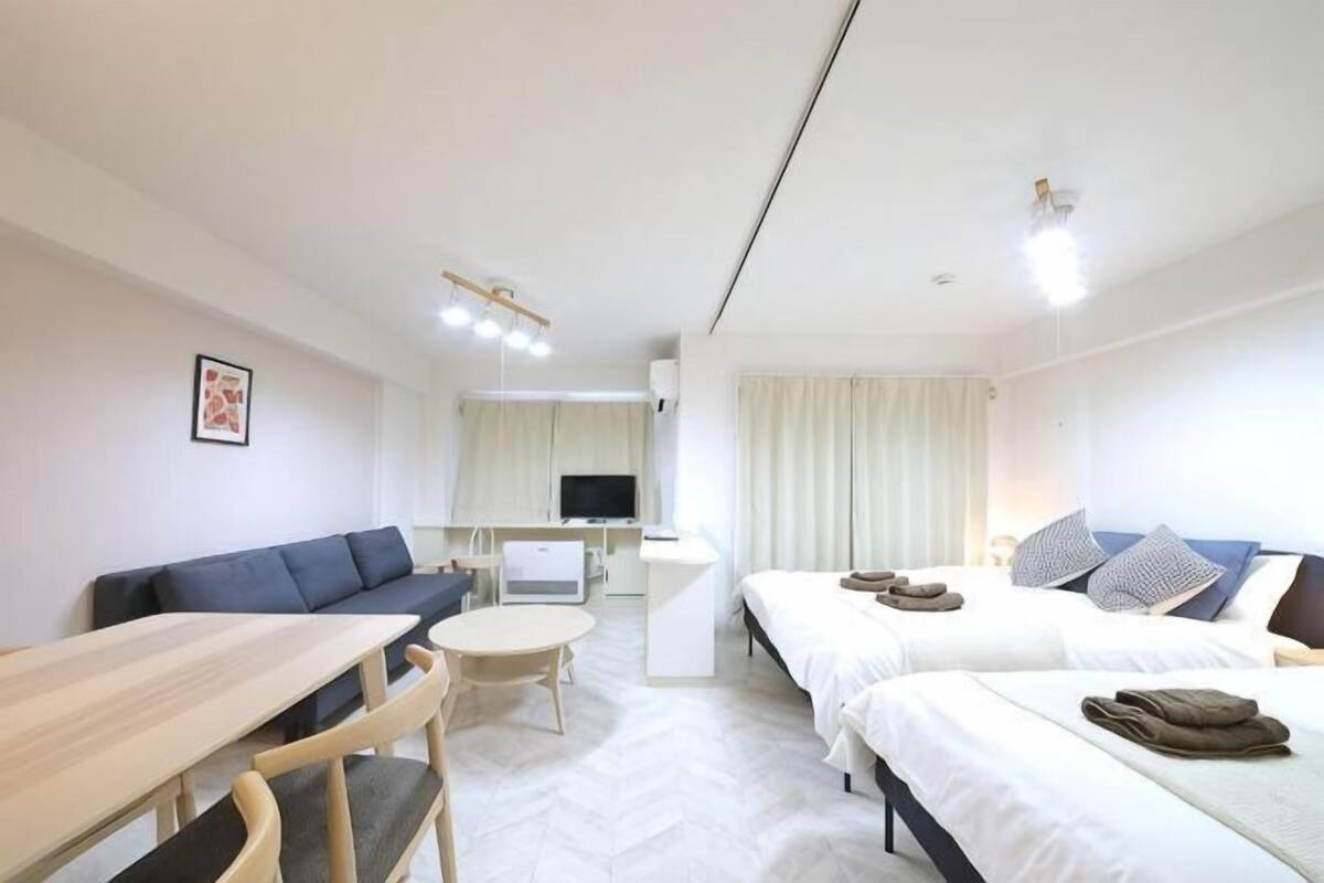 A hotel room with a sofa, a dining table, a TV, a bed, and a small kitchen area.