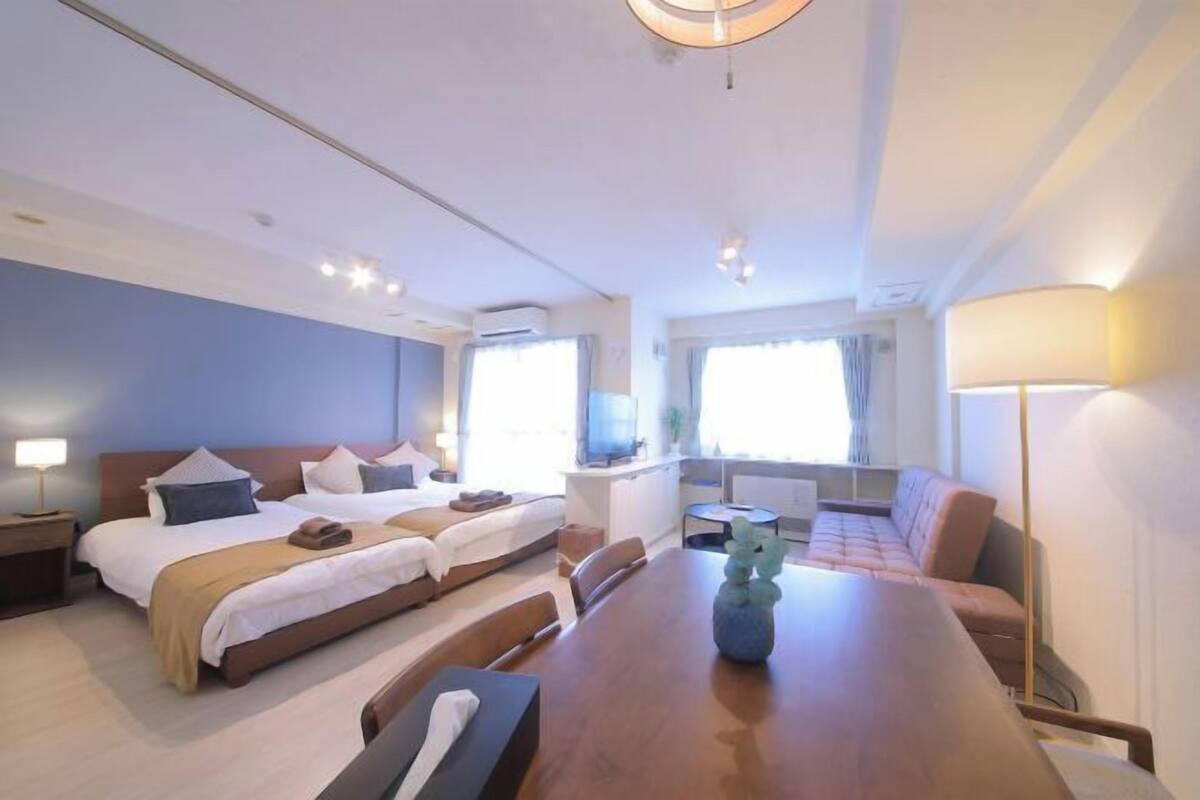 A hotel room with two beds, a dining table, a sofa, a TV, and a window.