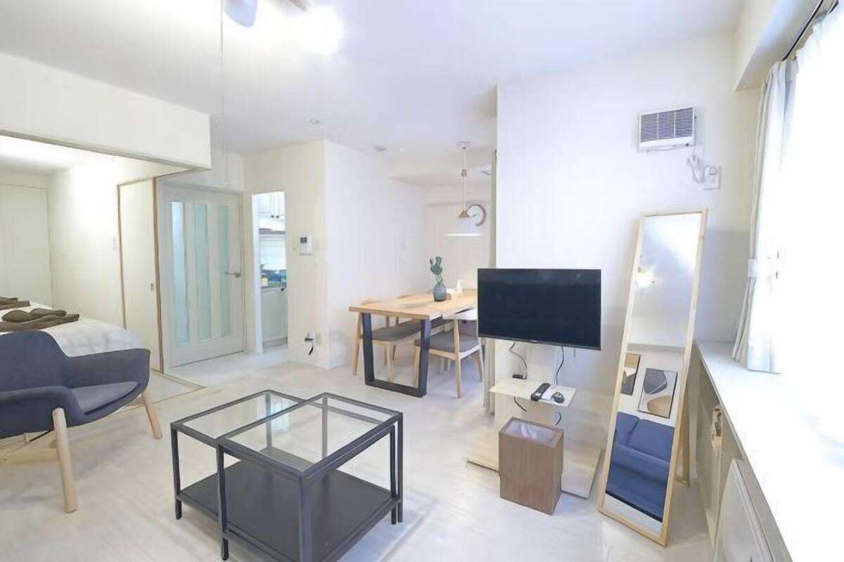 A modern living room with a glass coffee table, a sofa, a TV, and a dining area.