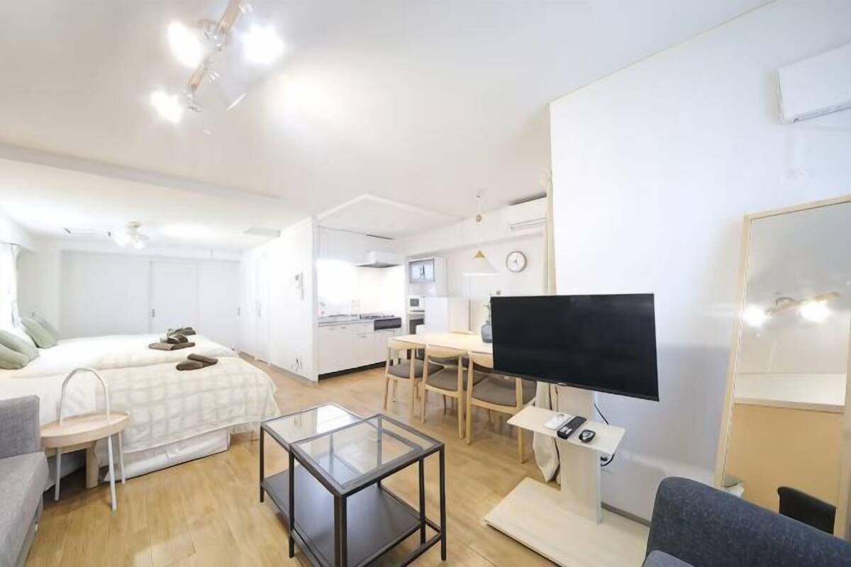 A modern, well-lit room with a bed, a desk, a TV, and a mirror.