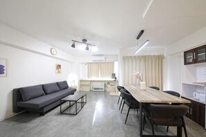 A modern living room with a sofa, dining table, chairs, and a kitchen area in the background. - Northern Hills Minami 6 (Sapporo)