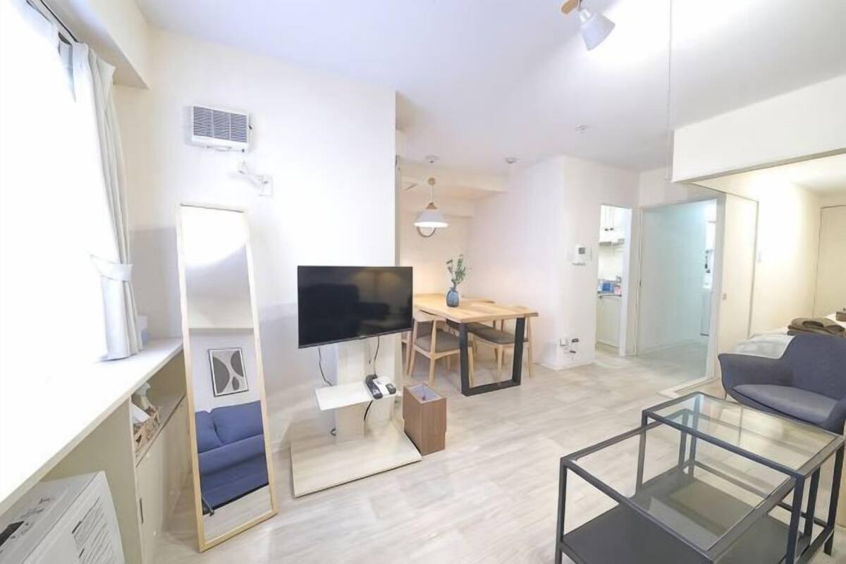 A modern living room with a flat-screen TV, a sofa, a glass coffee table, and a dining area with a table and chairs.