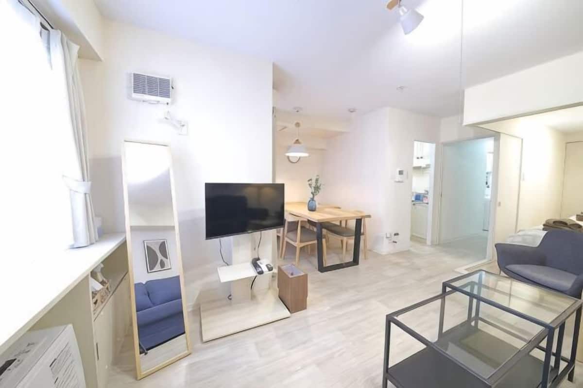 Una sala de estar moderna con una televisión de pantalla plana, un sofá, una mesa de centro de vidrio y un comedor con una mesa y sillas.