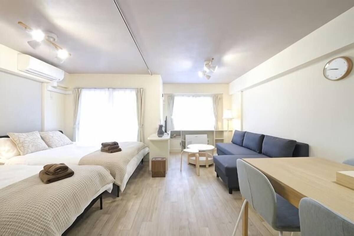 A hotel room with two beds, a sofa, a dining table, and a small desk.