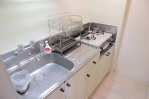 A kitchen with a stainless steel sink, a dish rack, a gas stove, and cabinets. - Northern Hills Minami 6 (Sapporo)