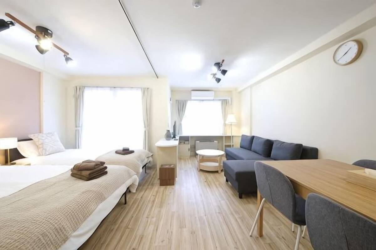 A hotel room with a bed, a sofa, a dining table, and a small kitchen area.