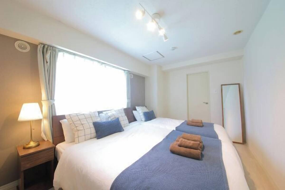 A hotel room with a bed, a nightstand, a lamp, a window with curtains, and a mirror.