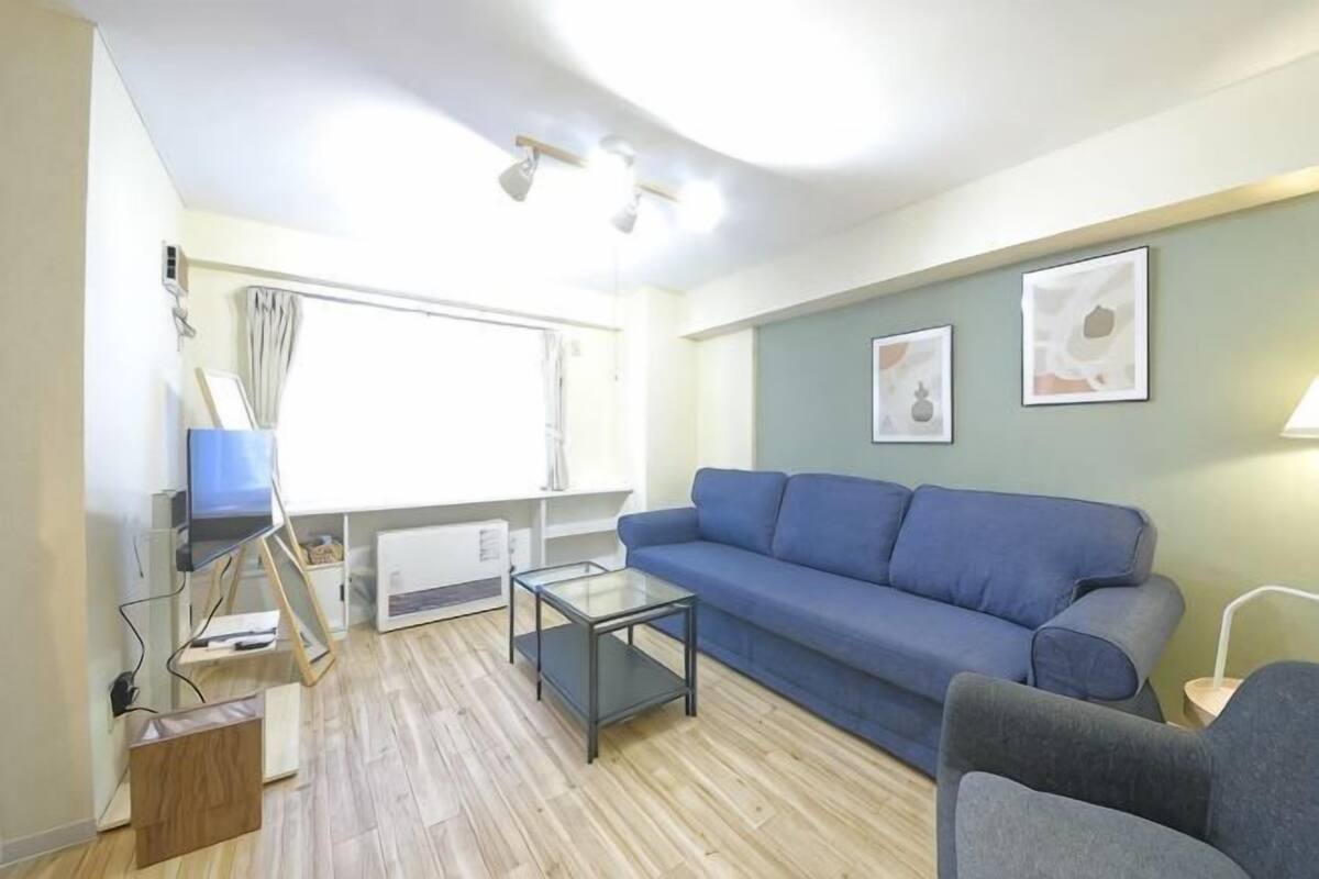 A living room with a blue sofa, a glass coffee table, a blue armchair, and a small table with a lamp.