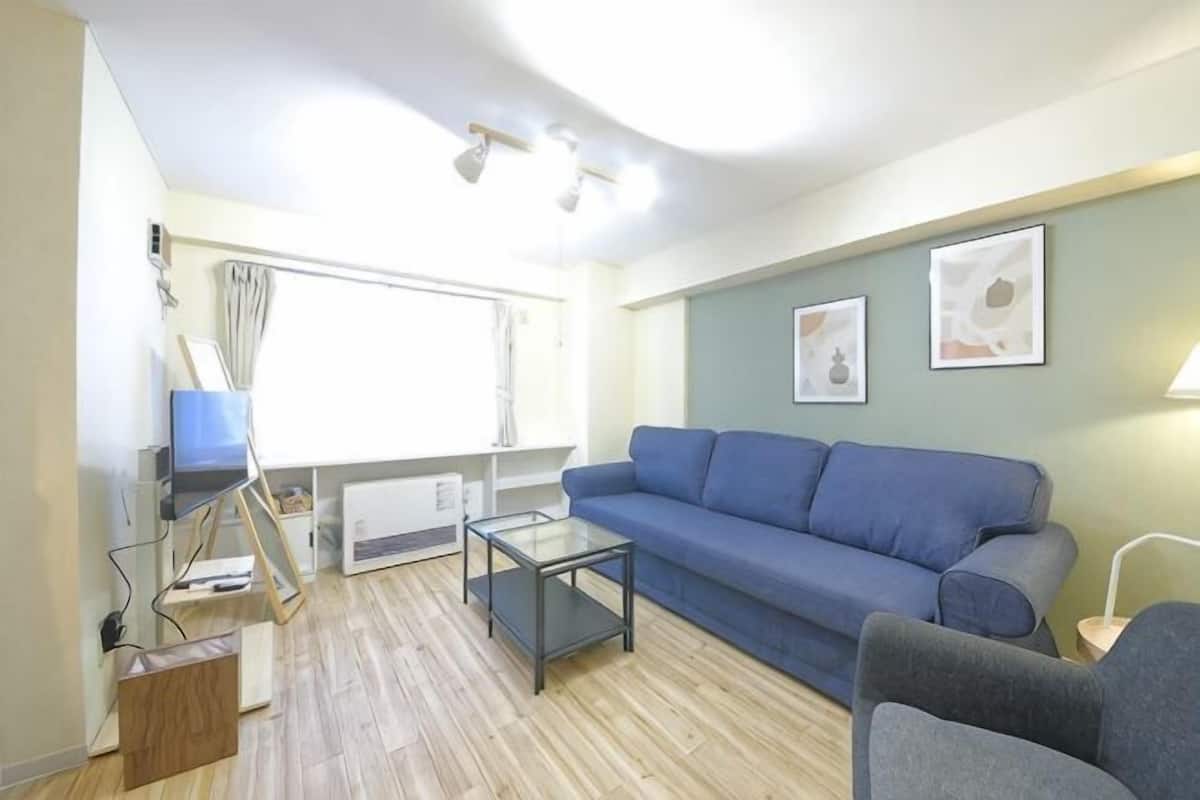 Una sala de estar con un sofá azul, una mesa de centro de vidrio, un sillón azul y una mesita con una lámpara.