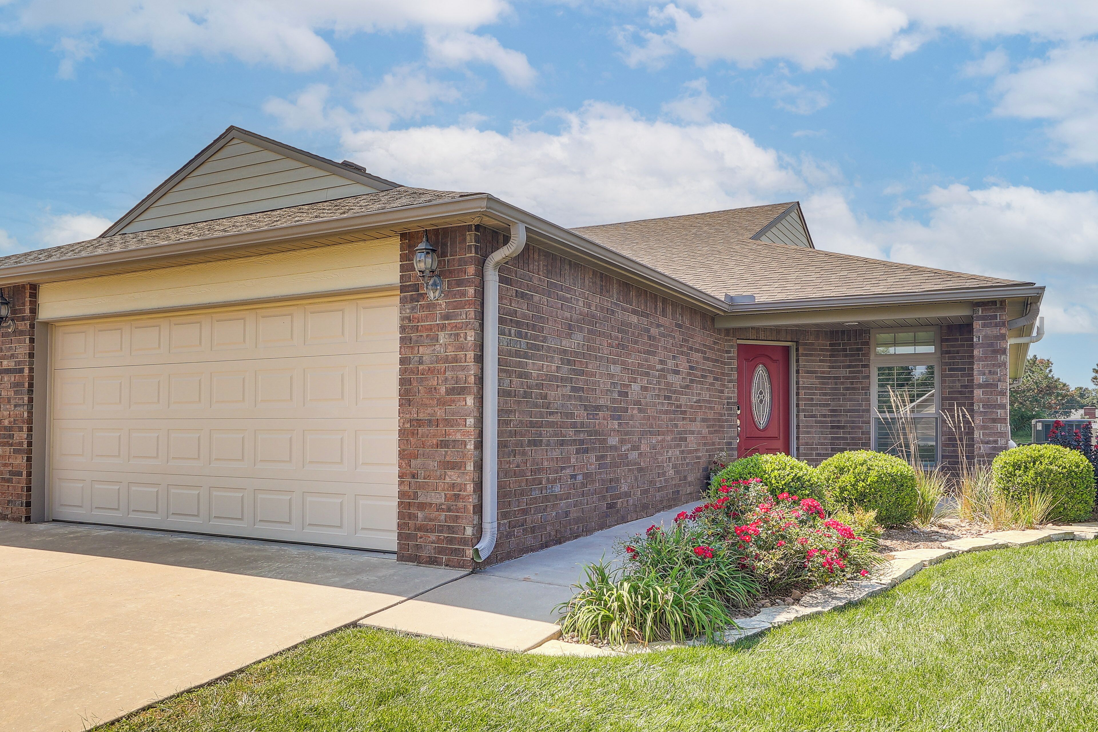 A residential house with a garage, brick exterior, and a well-maintained lawn with flowers.