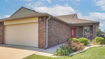 A residential house with a garage, brick exterior, and a well-maintained lawn with flowers.
