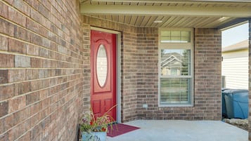 A red door with a decorative glass panel, a brick wall, and a window with a grid pattern.