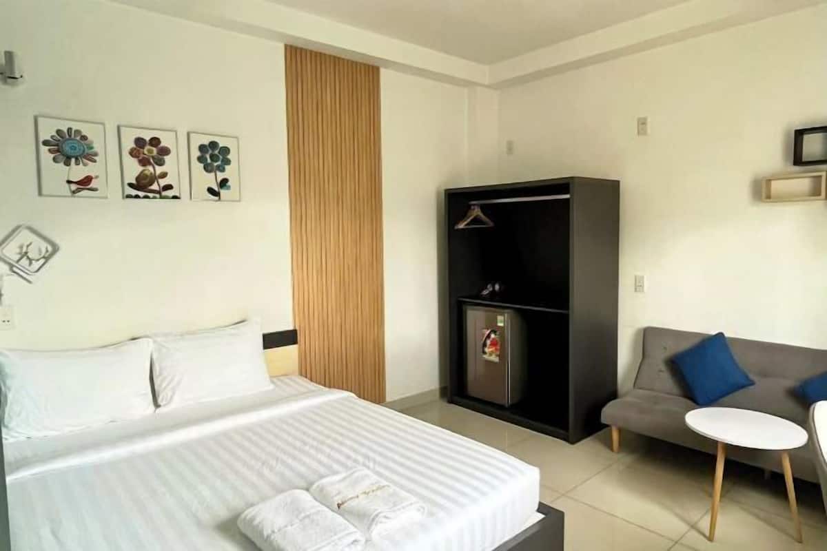 A hotel room with a bed, a sofa, a small table, a wardrobe, and wall art.