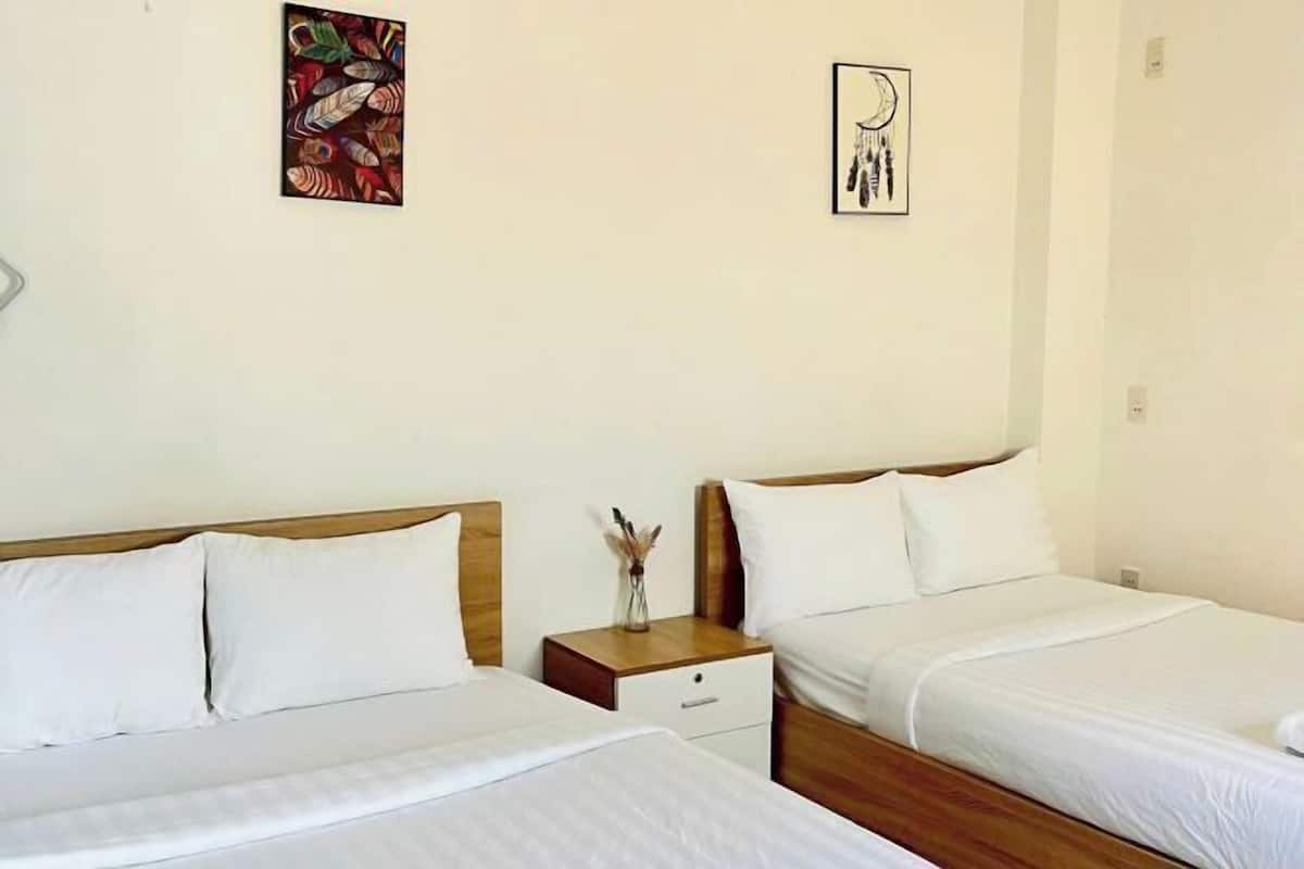 A hotel room with two single beds, a wooden headboard, a nightstand with a vase, and two wall art pieces.