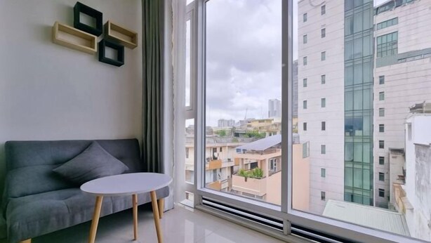A modern living room with a grey sofa, a small round table, and a large window offering a city view. - Atusy Boutique Hotel (Ho Chi Minh City)