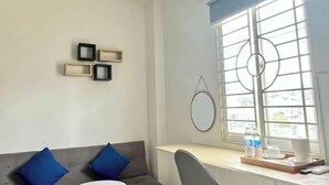 A room with a desk, a chair, a sofa with blue cushions, a window with a view, and wall-mounted picture frames. - Atusy Boutique Hotel (Ho Chi Minh City)