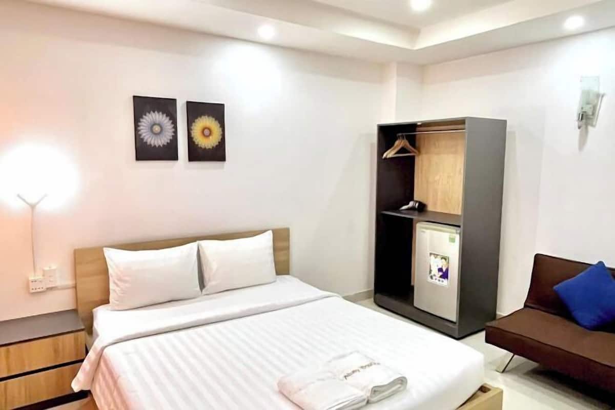 A hotel room with a bed, a wardrobe, a small fridge, a desk, and a sofa.