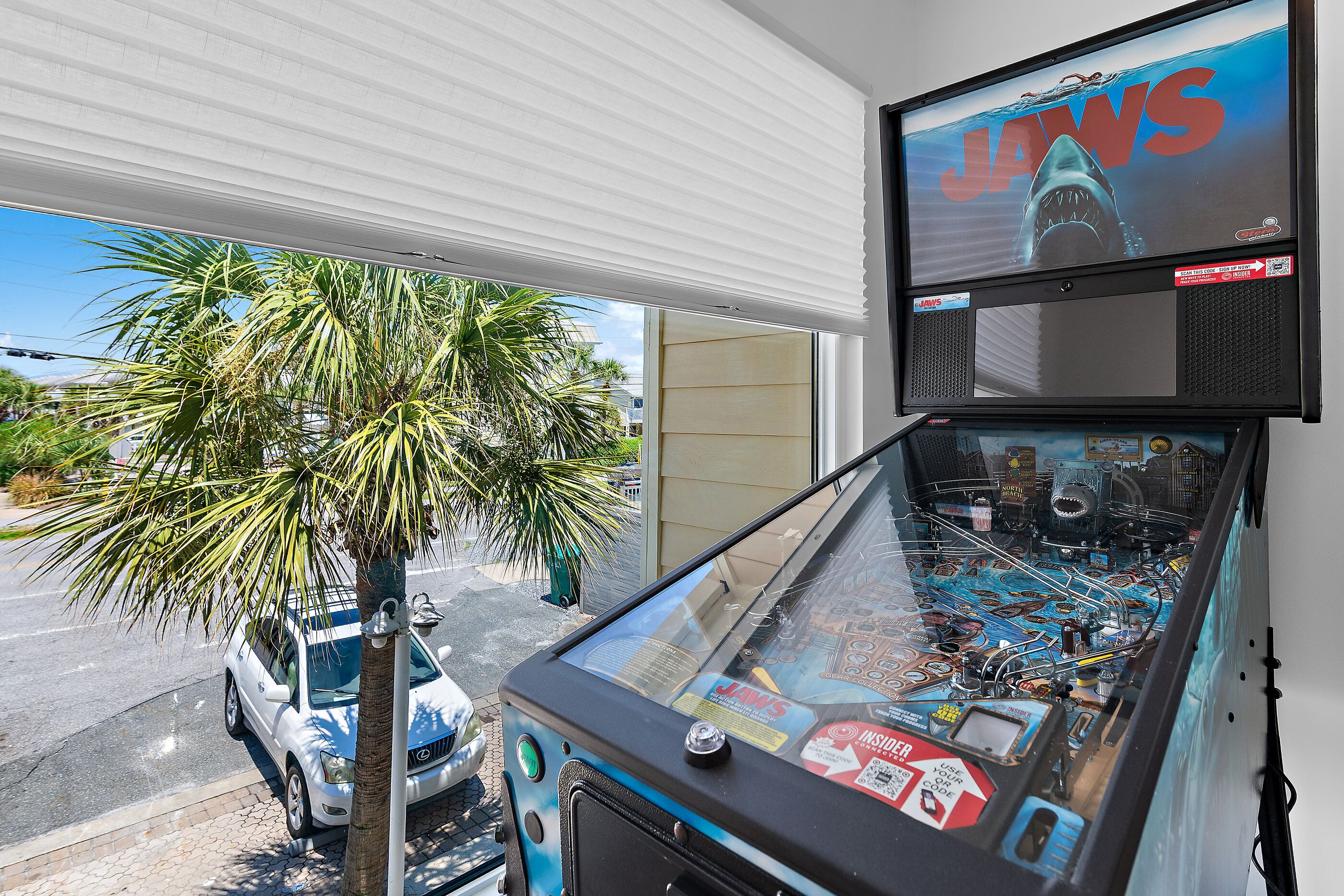 A pinball machine with a shark theme, a palm tree, and a parked car outside.
