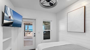 Un dormitorio con cama, televisor montado en la pared, ventana y puerta que da a un balcón.