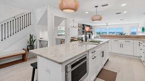 Una cocina moderna con armarios blancos, encimera de mármol e iluminación colgante.
