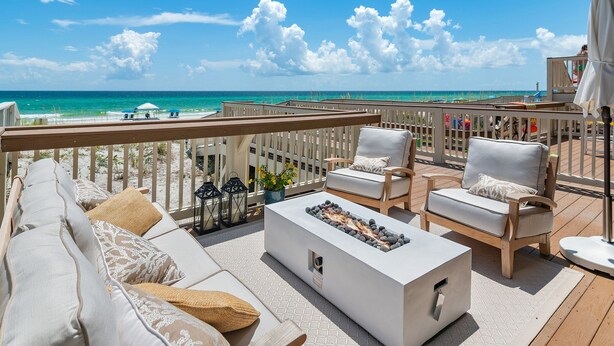 Una terraza con sofá, sillas, un brasero y vistas a la playa.