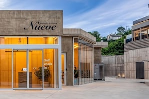 Un edificio moderno con facciata in vetro, un cartello con la scritta 'Nueve' e un cartello che indica 'Self check in'.
