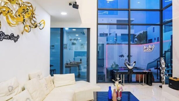 Un salon moderne avec un canapé blanc, une table basse noire agrémentée d’objets décoratifs et une grande fenêtre offrant une vue sur la ville.