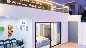Une villa moderne dotée d’une porte vitrée donnant sur une chambre, d’un coin salon avec des fauteuils et d’une enseigne au-dessus de la porte.