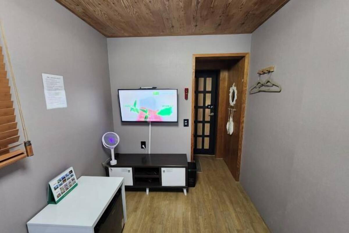 Un salon moderne avec un téléviseur à écran plat fixé au mur, une petite table avec un porte-revues et un plafond en bois.