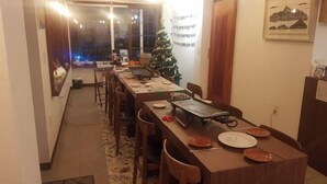 Un coin repas avec une longue table dressée pour le repas, un sapin de Noël et un tableau encadré accroché au mur.