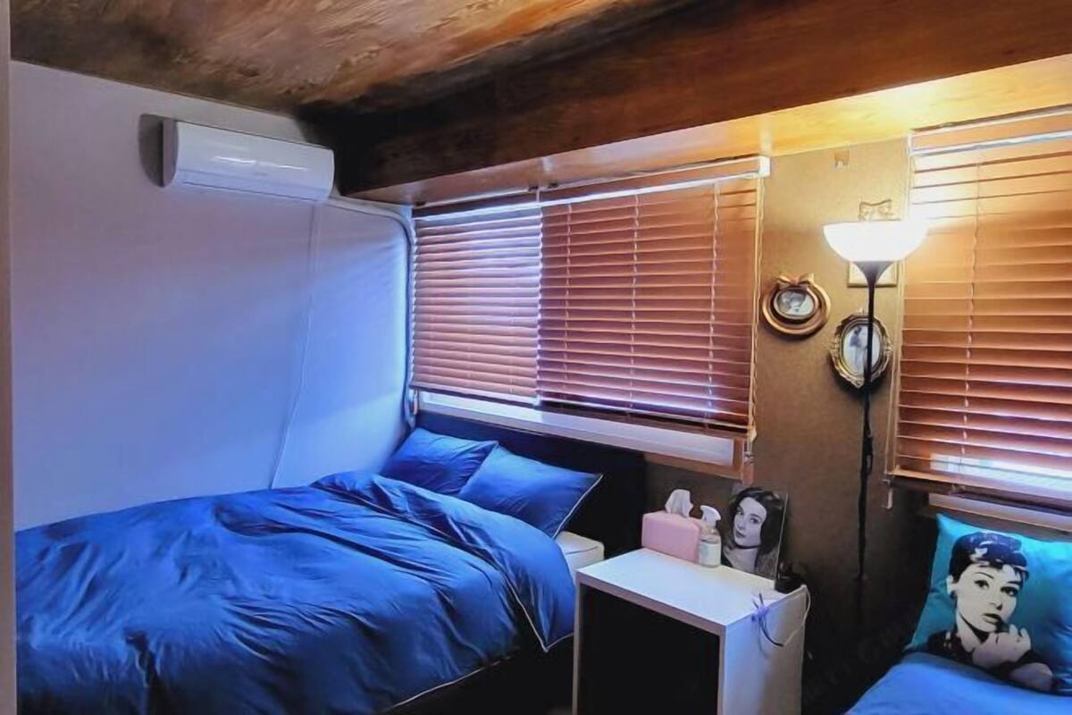 Une chambre à coucher avec un lit, une table de chevet, une lampe et des stores aux fenêtres.