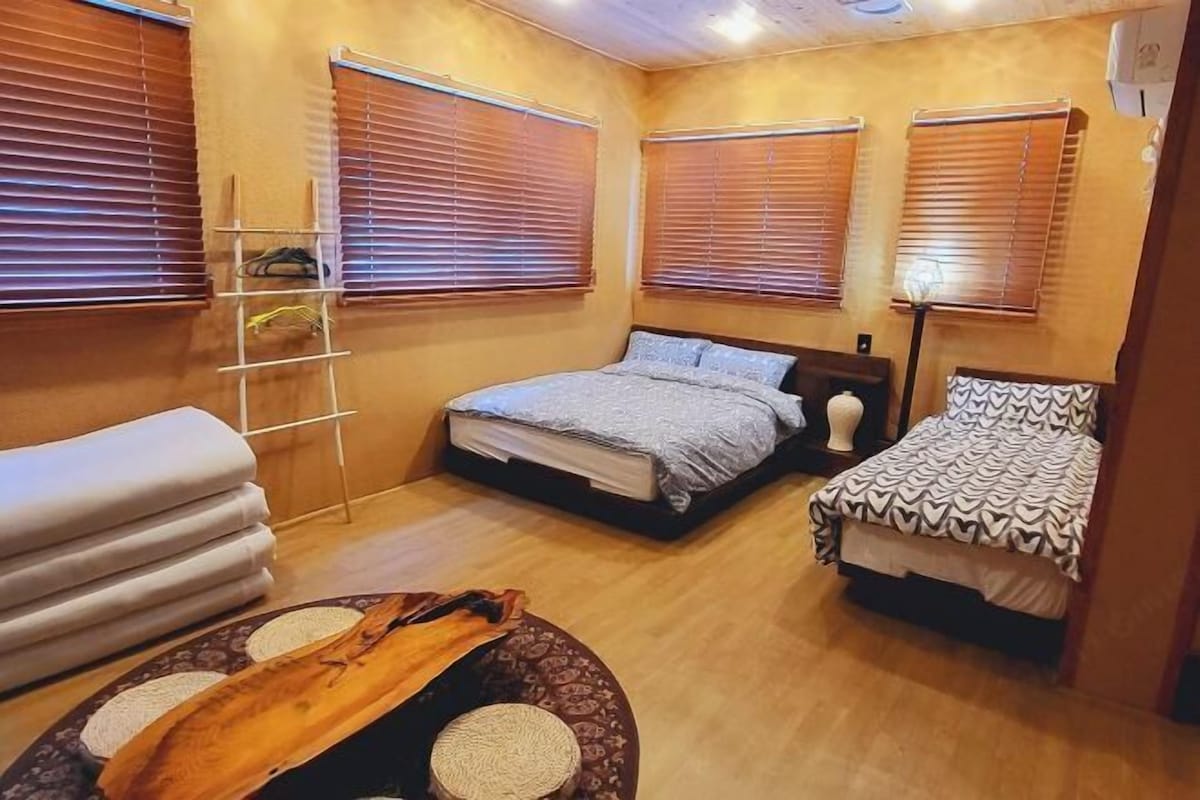 Une chambre avec deux lits, des stores en bois, une table de chevet, une lampe et une petite échelle.
