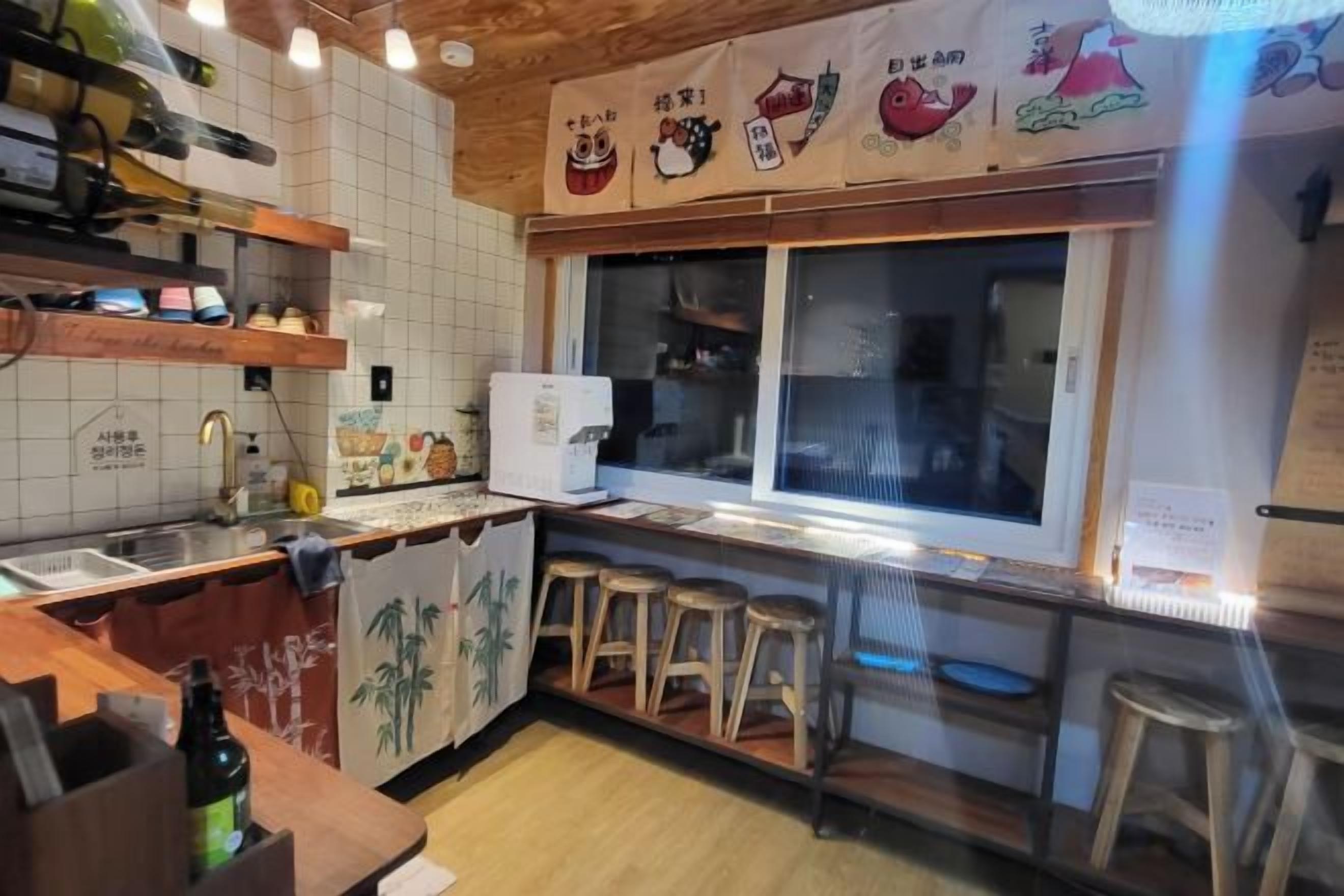 A kitchen with a refrigerator, wooden stools, and a window with a view.