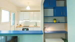 A modern kitchen with white and blue cabinets, a countertop with a sink, and a small table with a potted plant. - Ma de Bright Stay Attiki Metro (Athens)