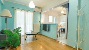 A modern living room with a sofa, a coffee table, and a potted plant. There is a kitchen area visible through an open doorway. - Ma de Bright Stay Attiki Metro (Athens)