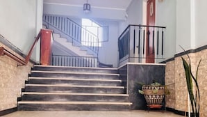 A staircase with a wooden handrail and a black railing, leading to a landing with a potted plant and a door. - Ma de Bright Stay Attiki Metro (Athens)