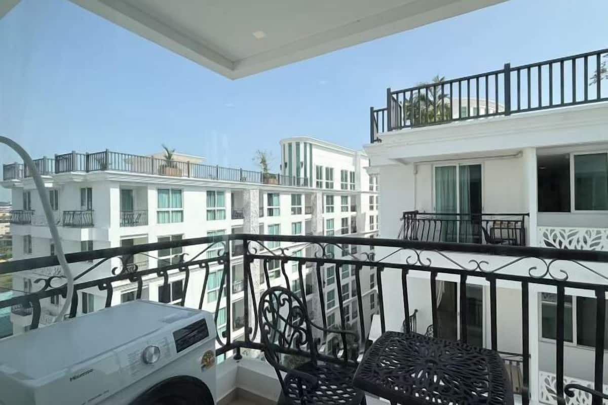 A balcony with a white appliance, black metal railing, and a view of adjacent buildings.