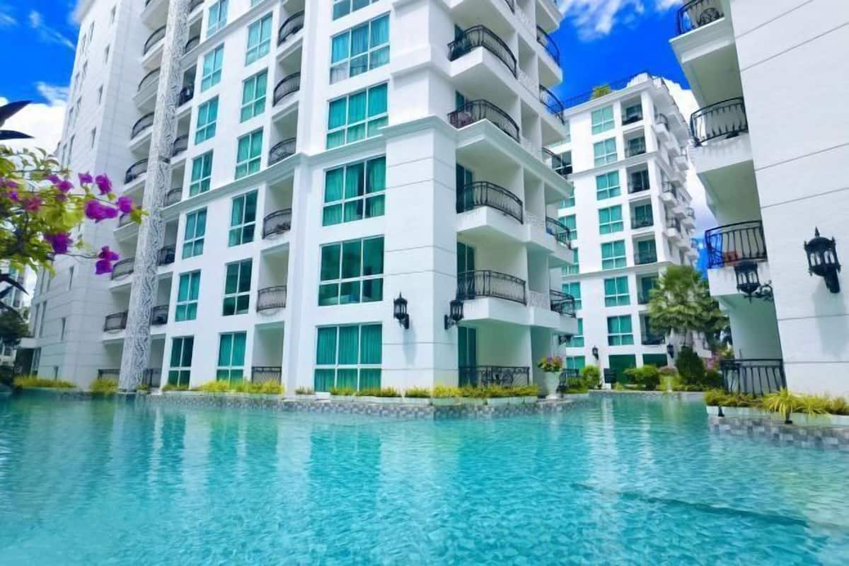 A multi-story hotel with a swimming pool in front.