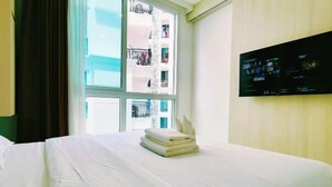 Ein Hotelzimmer mit einem Bett, einem Fenster mit Blick auf ein Gebäude und einem an der Wand befestigten Fernseher.