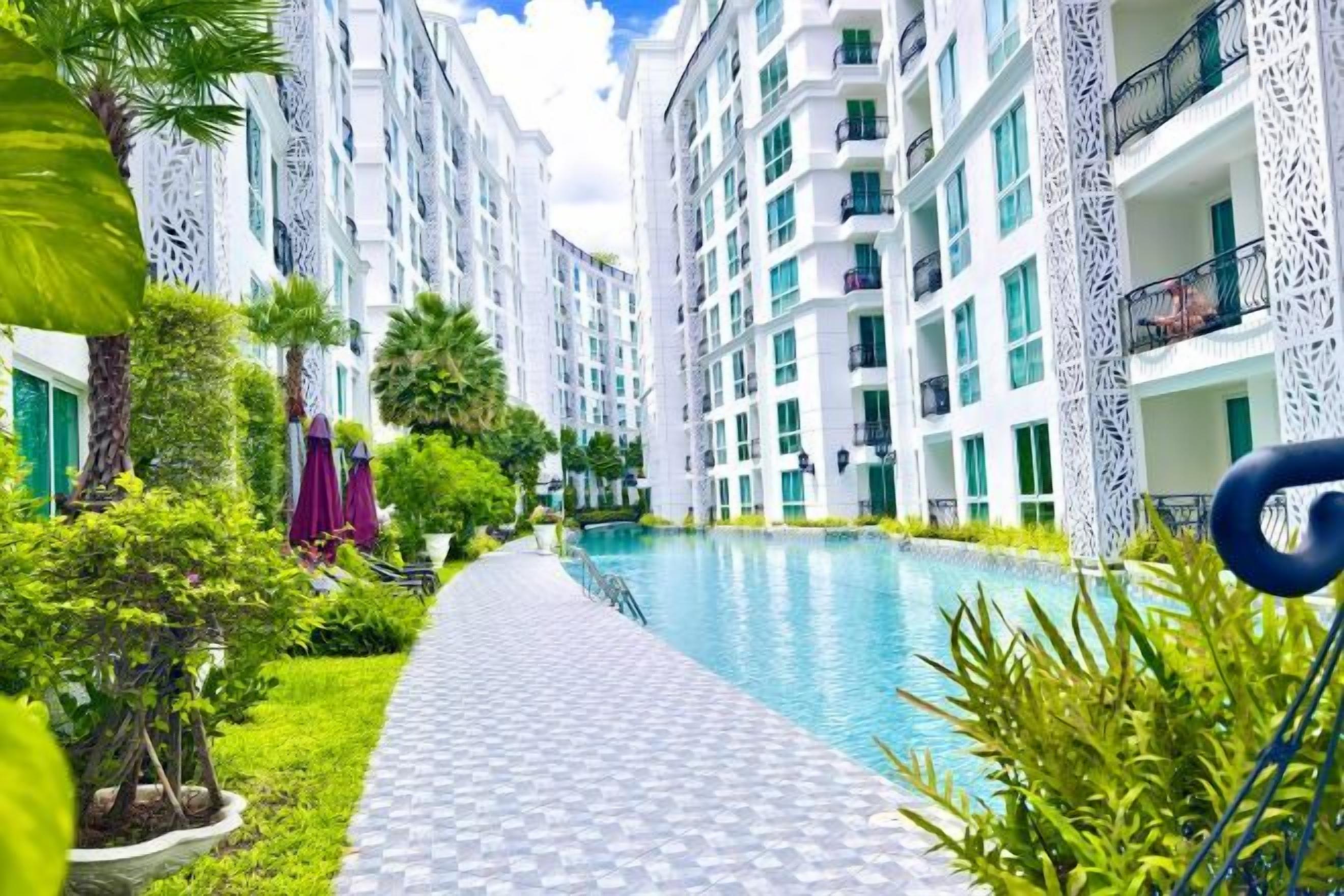 A swimming pool area with a pathway, surrounded by multi-story buildings with balconies.