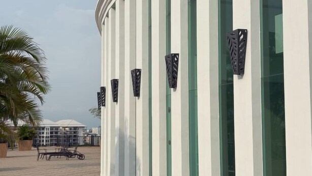 Ein modernes Gebäude mit vertikalen Streifen, Außenbestuhlung und einer Palme.