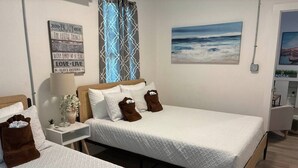 Une chambre avec deux lits, une table de chevet avec une lampe, un mur orné de citations inspirantes et un tableau représentant une plage.