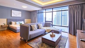 A modern hotel room with a bed, sofa, and coffee table. There is a large window with curtains and a view of buildings. - Anggun KLCC Spacious Studio Steps to Monorail & LRT FREE Parking (Kuala Lumpur)