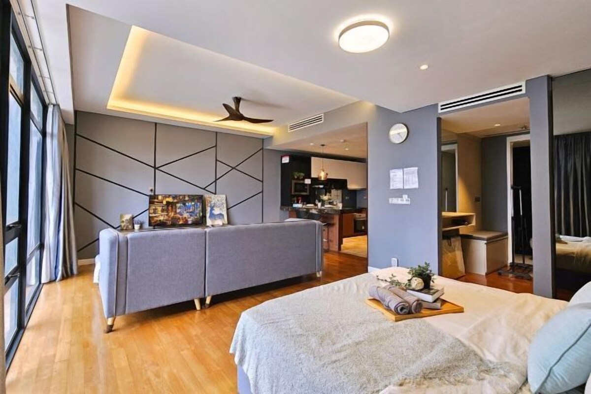 A modern hotel room with a bed, a sofa, a desk, and a view of the kitchen.