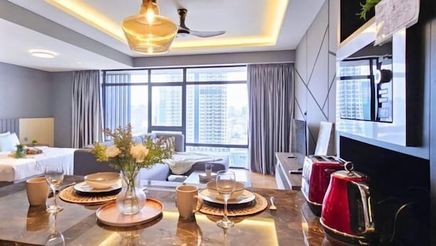 A modern hotel room with a dining area, a bed, and a large window with a city view. - Anggun KLCC Spacious Studio Steps to Monorail & LRT FREE Parking (Kuala Lumpur)