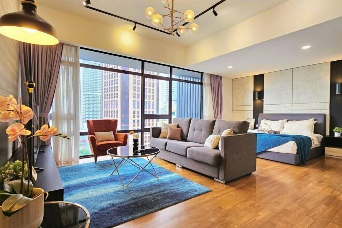 A modern hotel room with a large window, a sofa, a bed, and a small table.