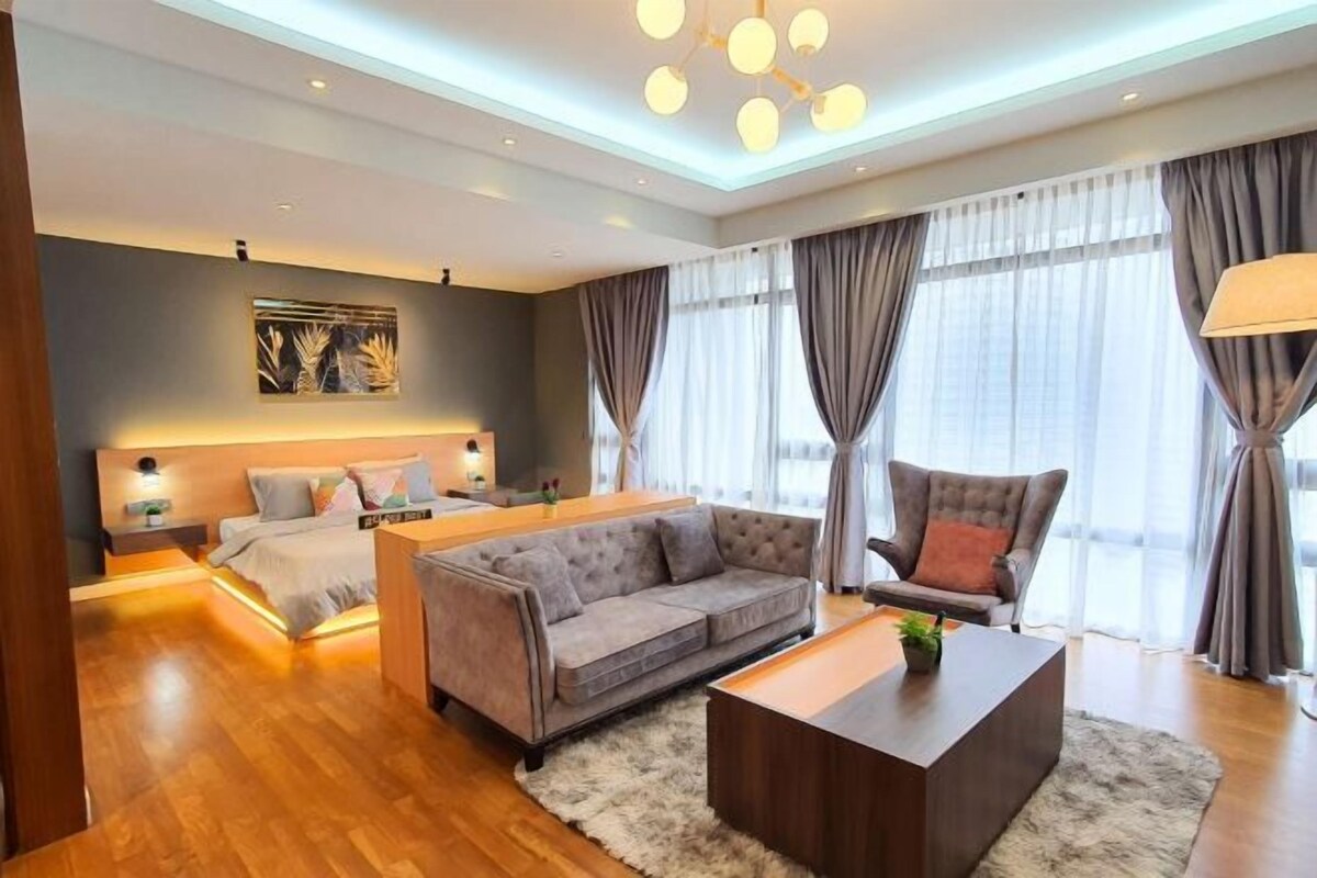 A modern hotel room with a bed, a sofa, a coffee table, and a large window with curtains.