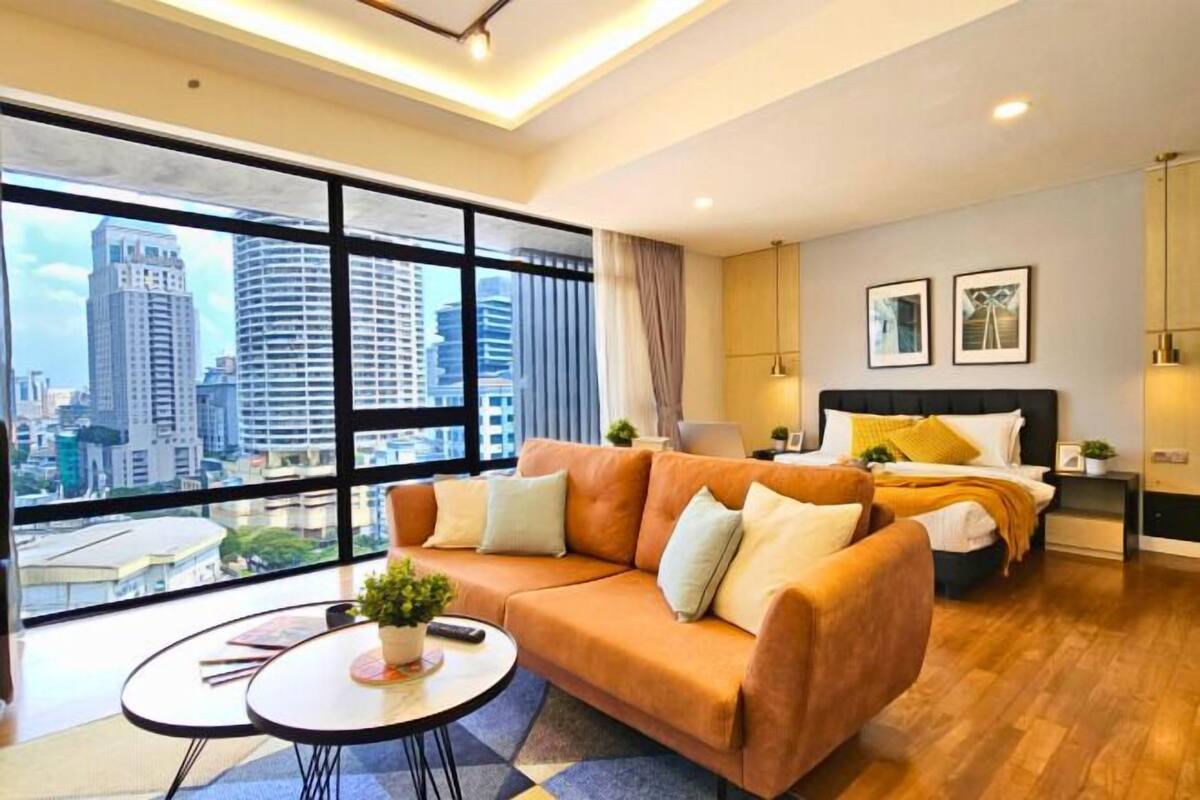 A modern hotel room with a large window, a sofa, a bed, and a small table with a plant.